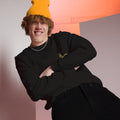 Person wearing a black outfit with a yellow beanie against a colorful geometric background