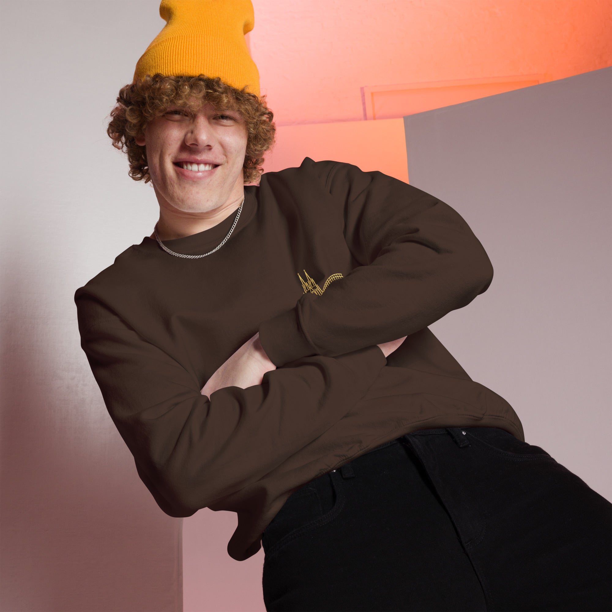 Person wearing a brown  Köln sweater and yellow beanie against a geometric background