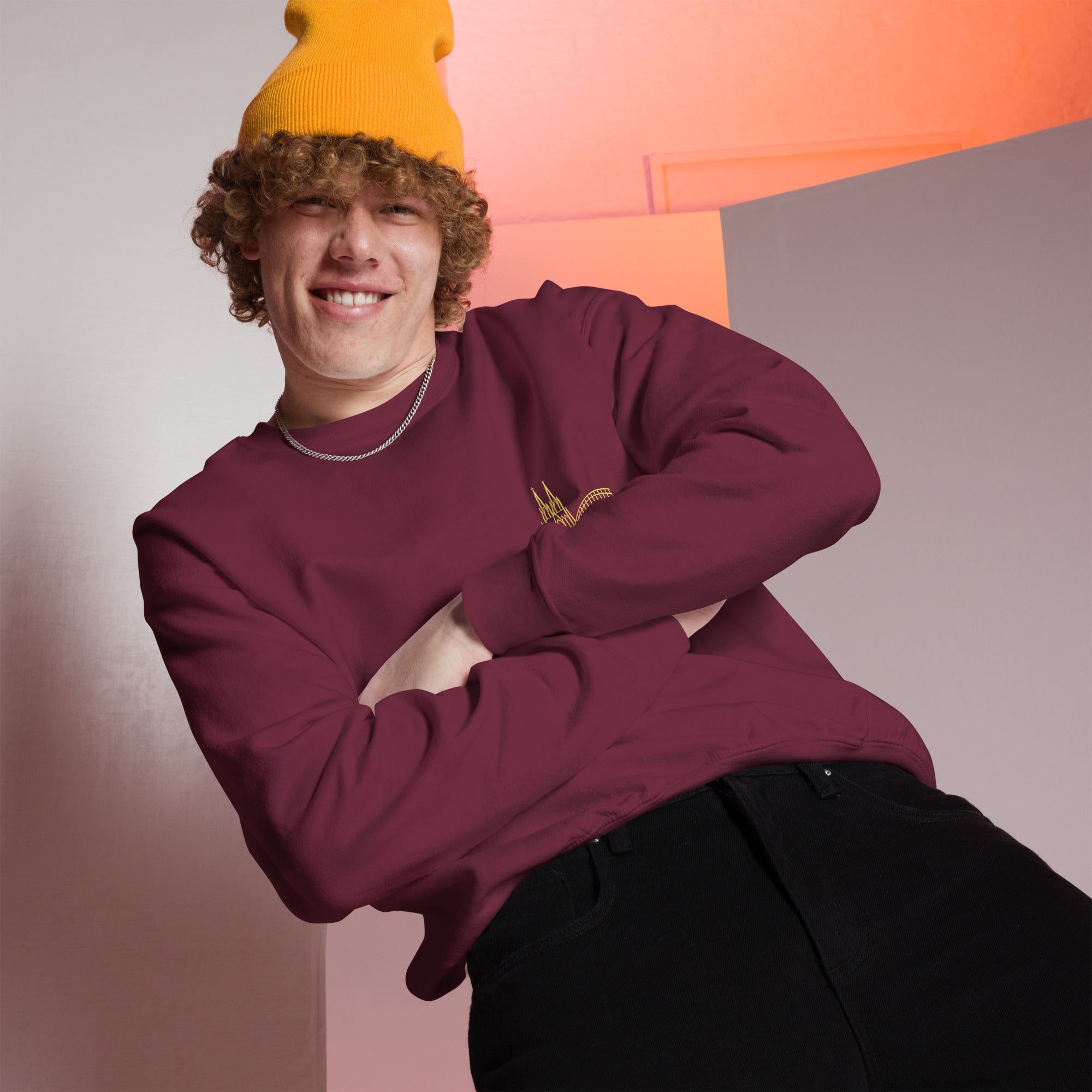 Person wearing a maroon Köln sweatshirt and yellow beanie against a geometric background