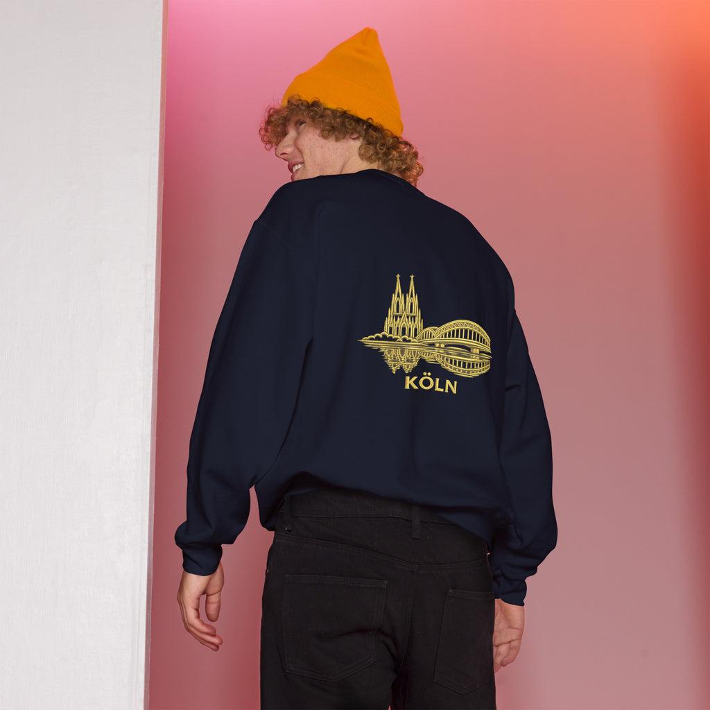 Person wearing a navy sweatshirt with a yellow 'Köln' design on the back, standing against a gradient pink and white background.