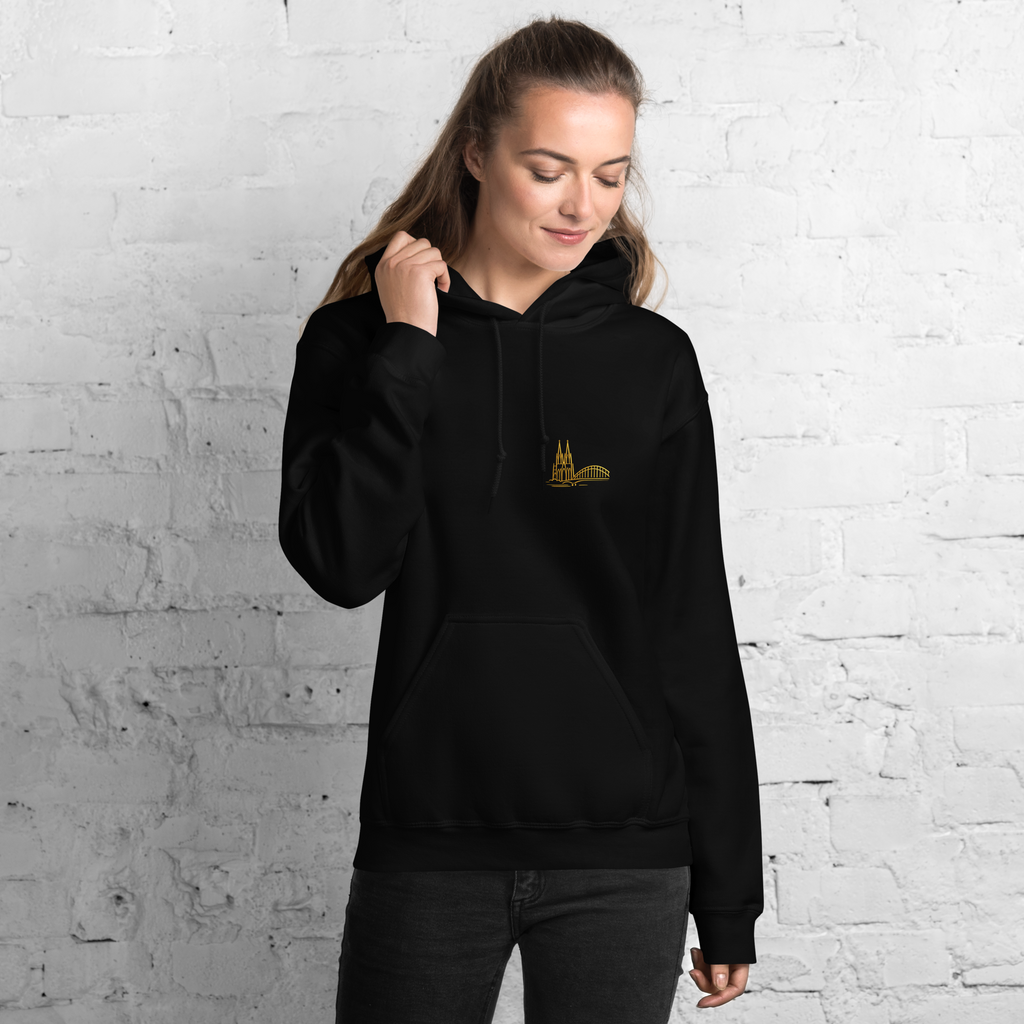 Person wearing a black hoodie with a logo against a white brick wall