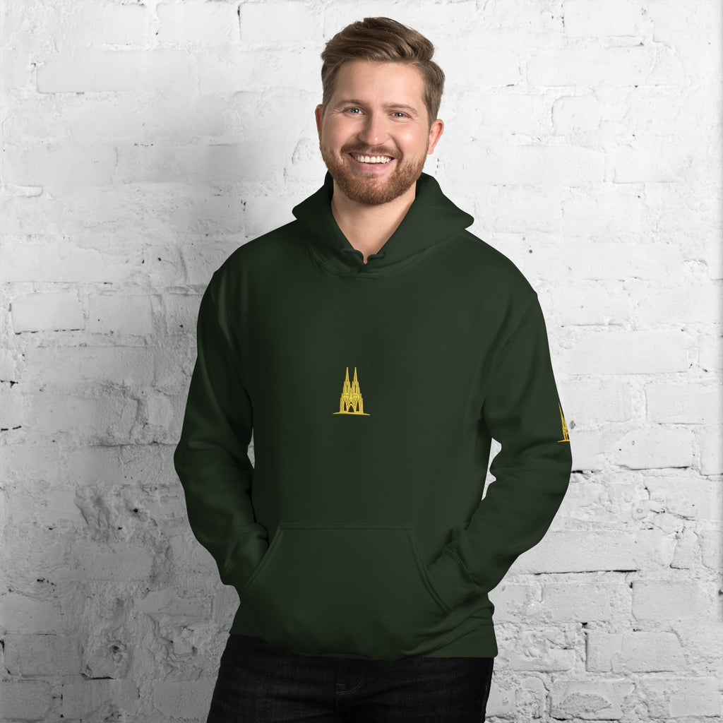 Man wearing a FOREST green hoodie with a GOLD KÖLN emblem against a white brick wall.